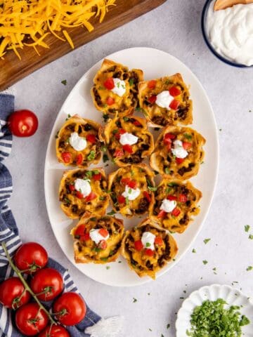 Mini Taco Cups on a platter with sour cream, tomatoes and cilantro from above