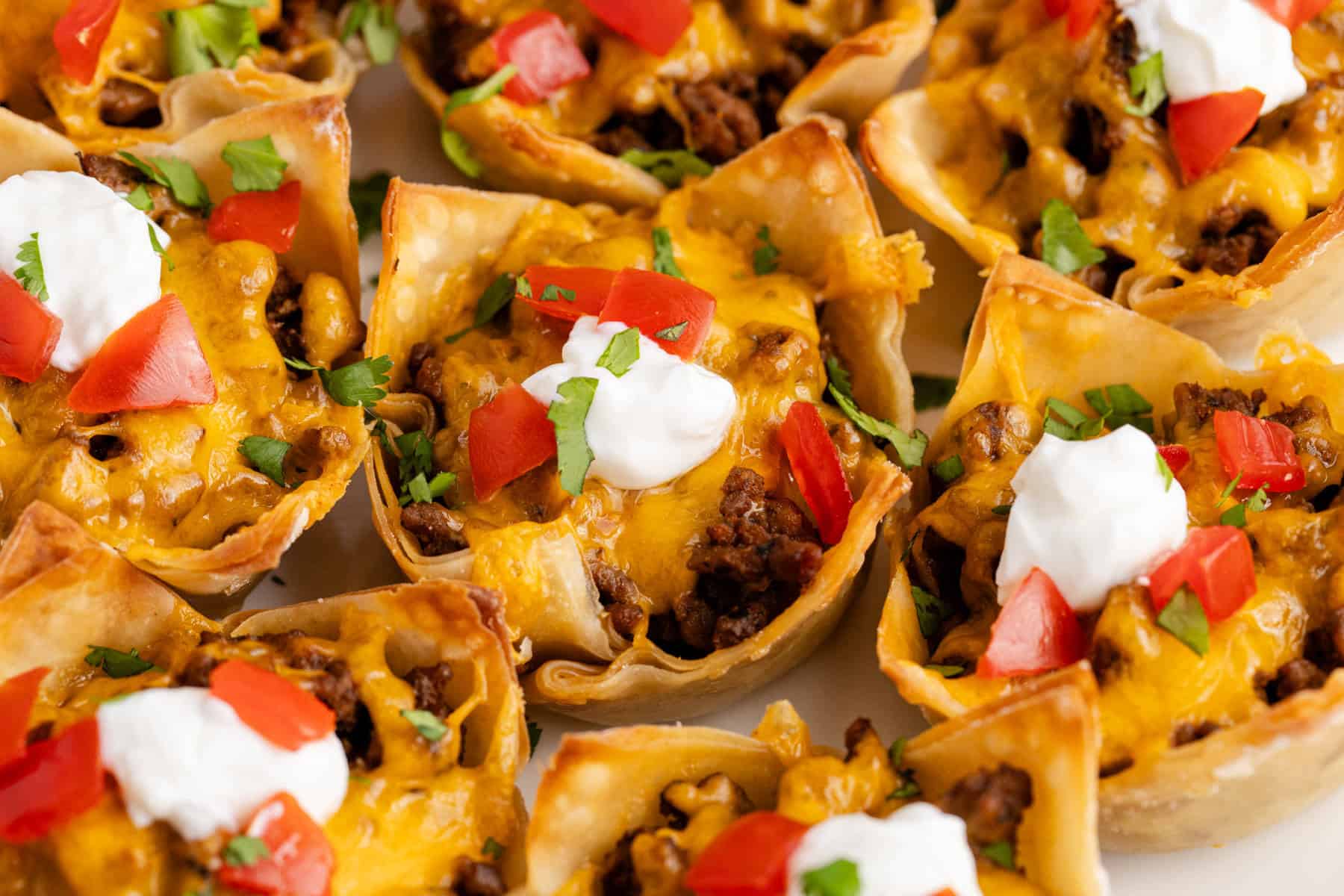 Mini Taco Cups on a platter with sour cream, tomatoes and cilantro