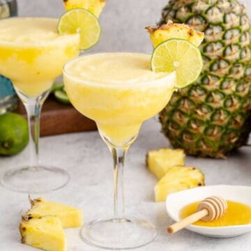 Frozen Non Alcoholic Pineapple Margaritas on a counter with a pineapple in the back and honey to the side