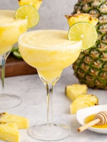 Frozen Non Alcoholic Pineapple Margaritas on a counter with a pineapple in the back and honey to the side
