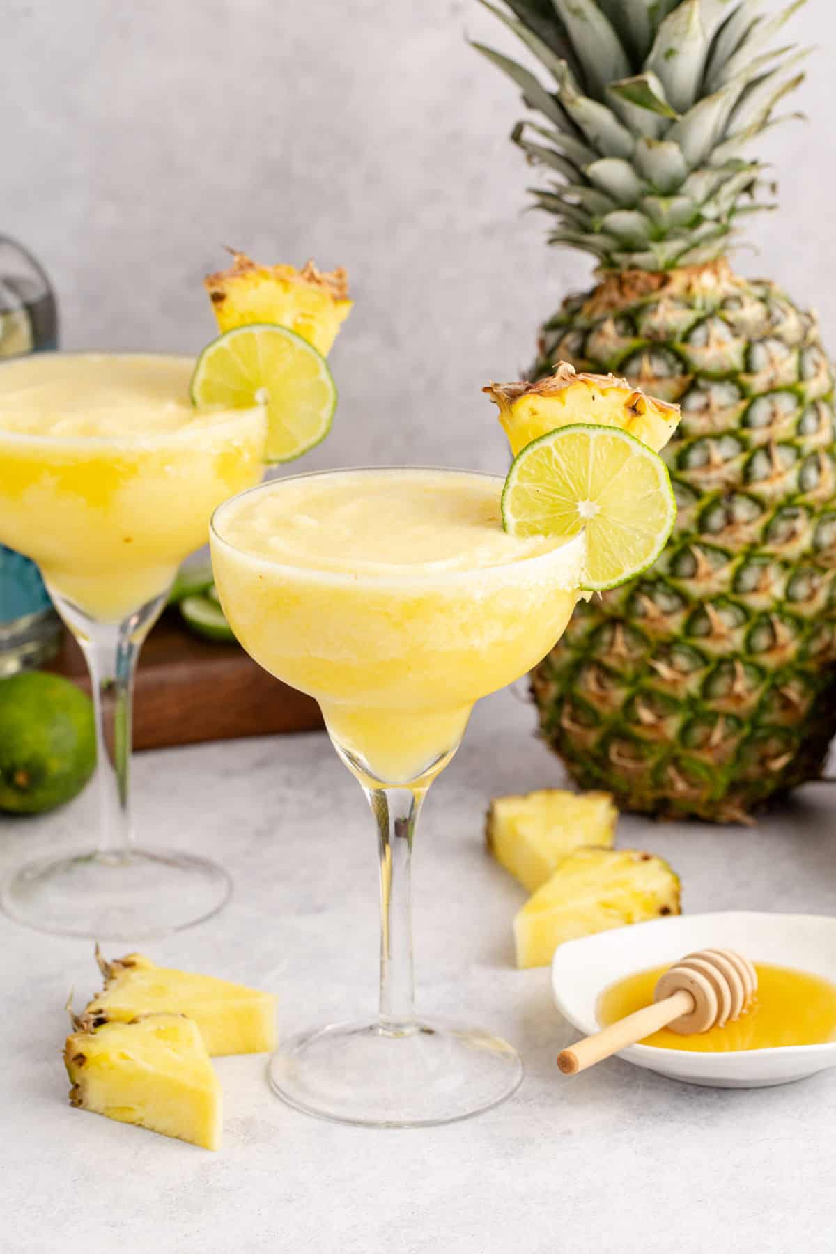Frozen Non Alcoholic Pineapple Margaritas on a counter with a pineapple in the back and honey to the side