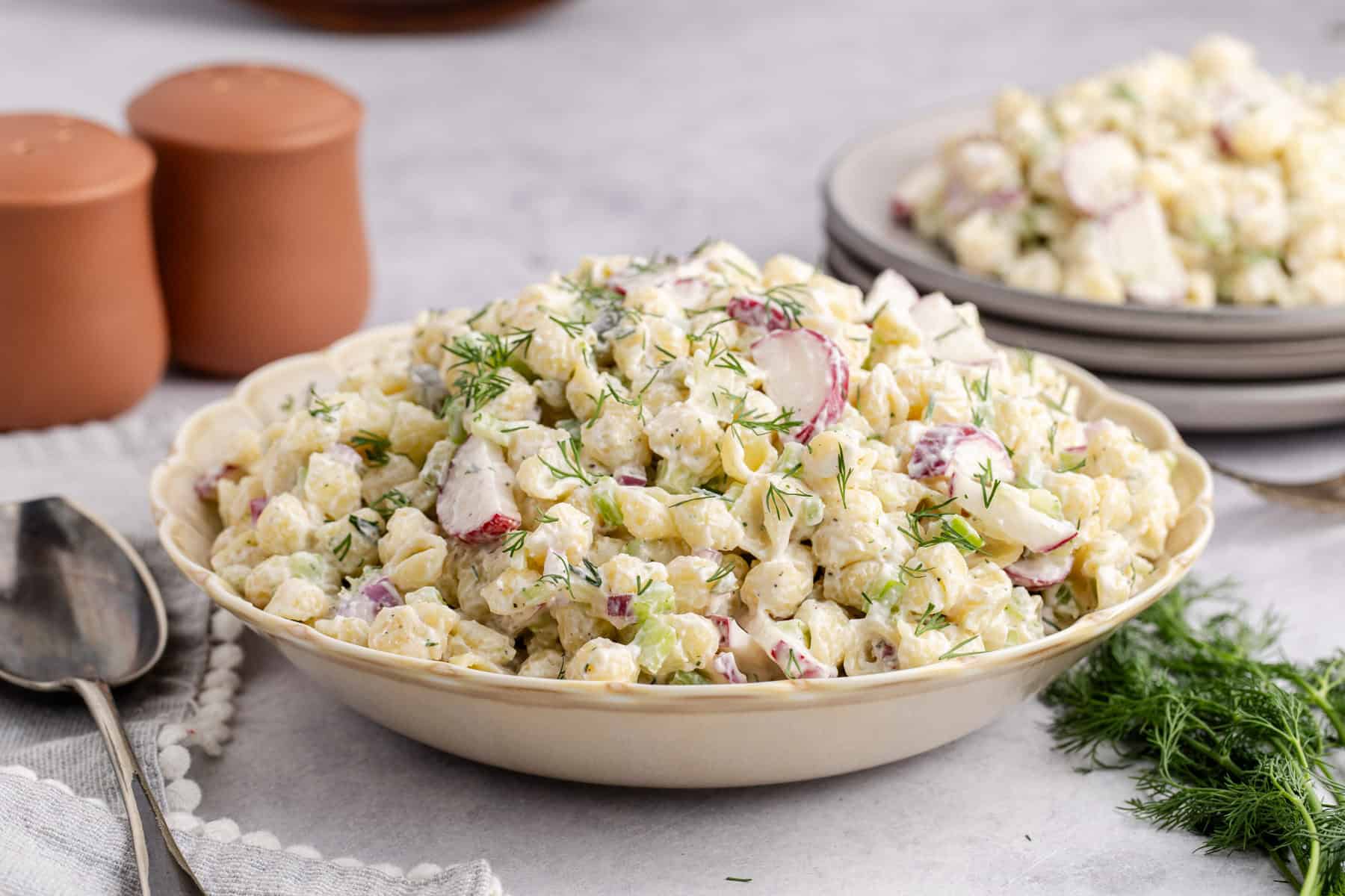 Pasta Salad with Fresh Dill in a serving bowl with a full plate in the background