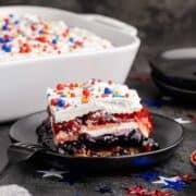 Red White and Blue Dessert Lasagna slice on a plate with the rest in the background