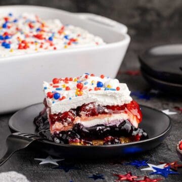 Red White and Blue Dessert Lasagna slice on a plate with the rest in the background