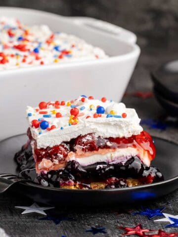 Red White and Blue Dessert Lasagna slice on a plate with the rest in the background