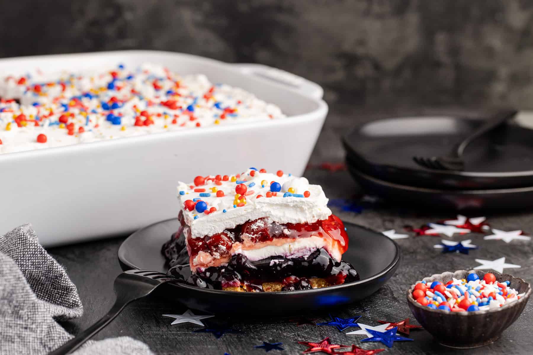 Red White and Blue Dessert Lasagna slice on a plate with the rest in the background