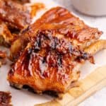 BBQ Ribs on parchment paper with sauce in the background