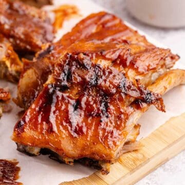 BBQ Ribs on parchment paper with sauce in the background
