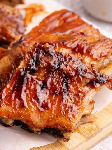 BBQ Ribs on parchment paper with sauce in the background