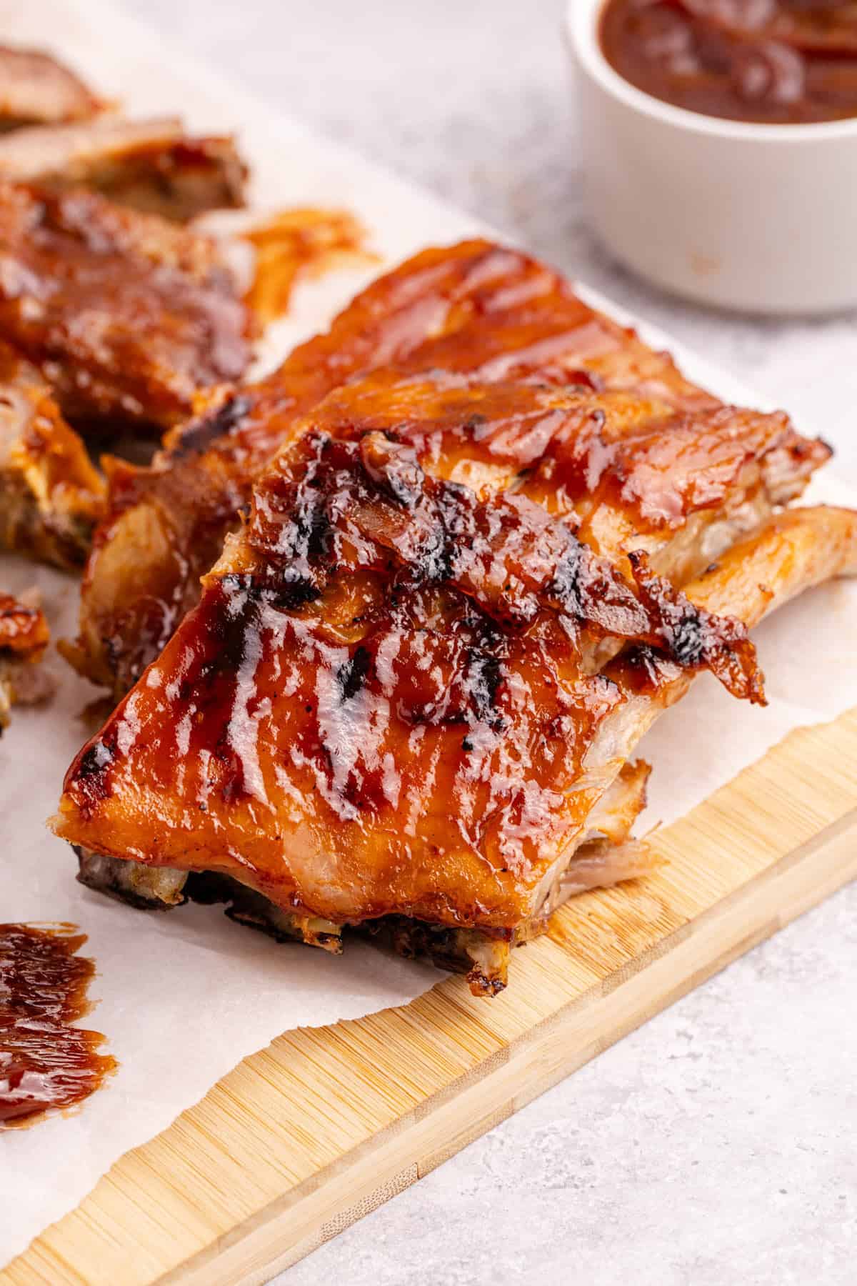 BBQ Ribs on parchment paper with sauce in the background