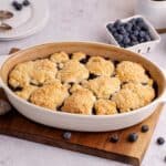 Blueberry Cobbler baked in an oval dish with blueberries in the back