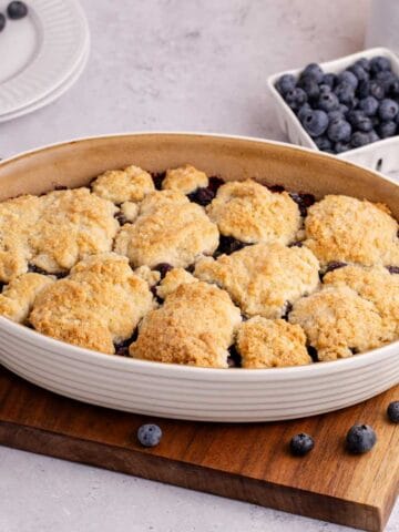 Blueberry Cobbler baked in an oval dish with blueberries in the back
