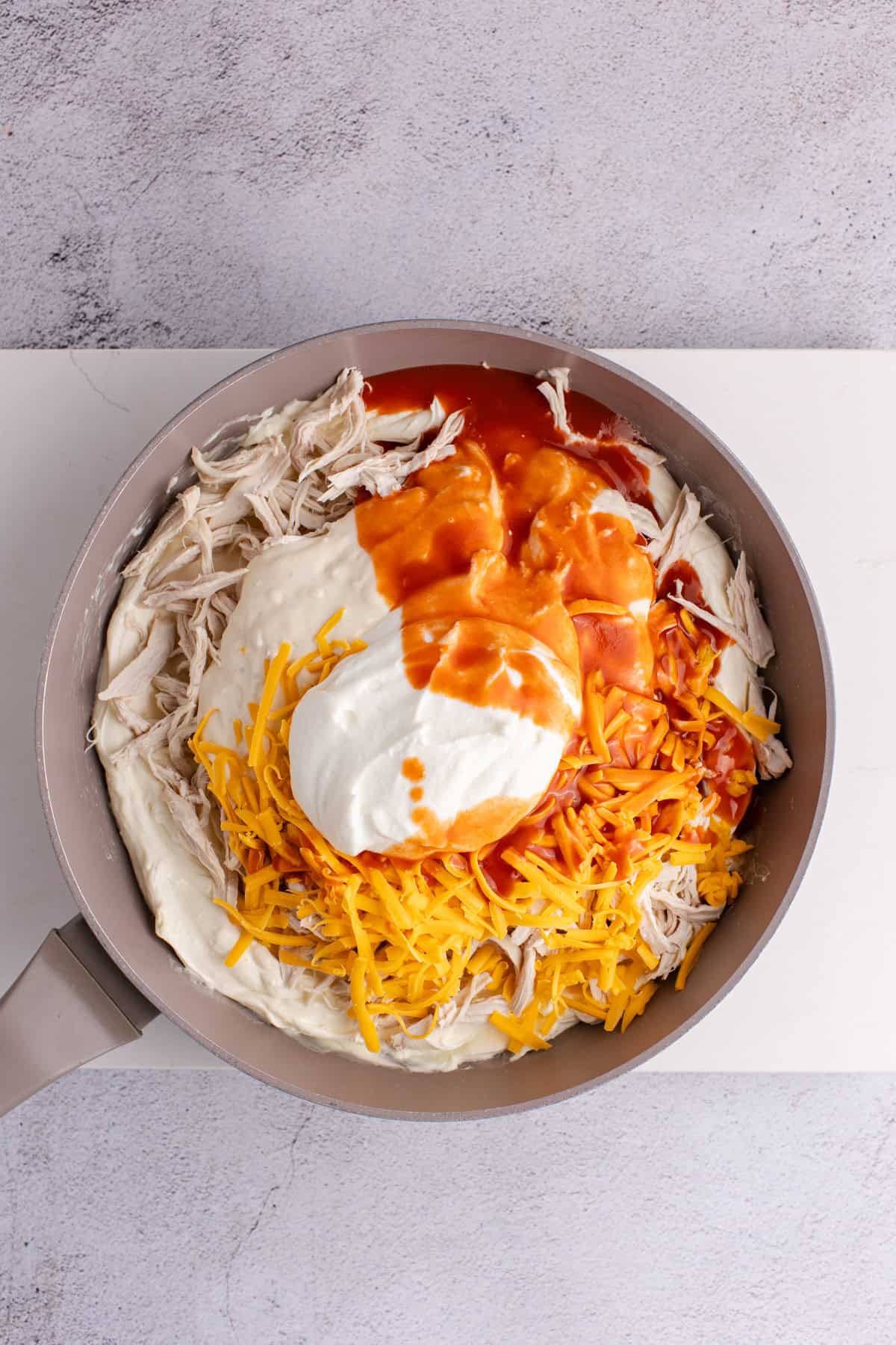 Buffalo Chicken Wing Dip with Rotisserie Chicken being made in a skillet before a baking dish