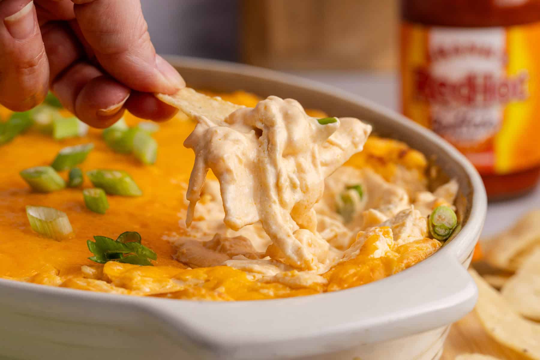Buffalo Chicken Wing Dip with Rotisserie Chicken baked in a dish with a scoop being taken with a corn chip