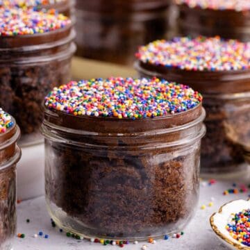 Chocolate Viral Dot Cakes in jars on a counter with sprinkles all around