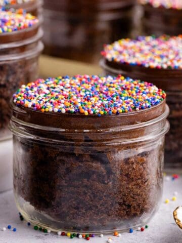 Chocolate Viral Dot Cakes in jars on a counter with sprinkles all around