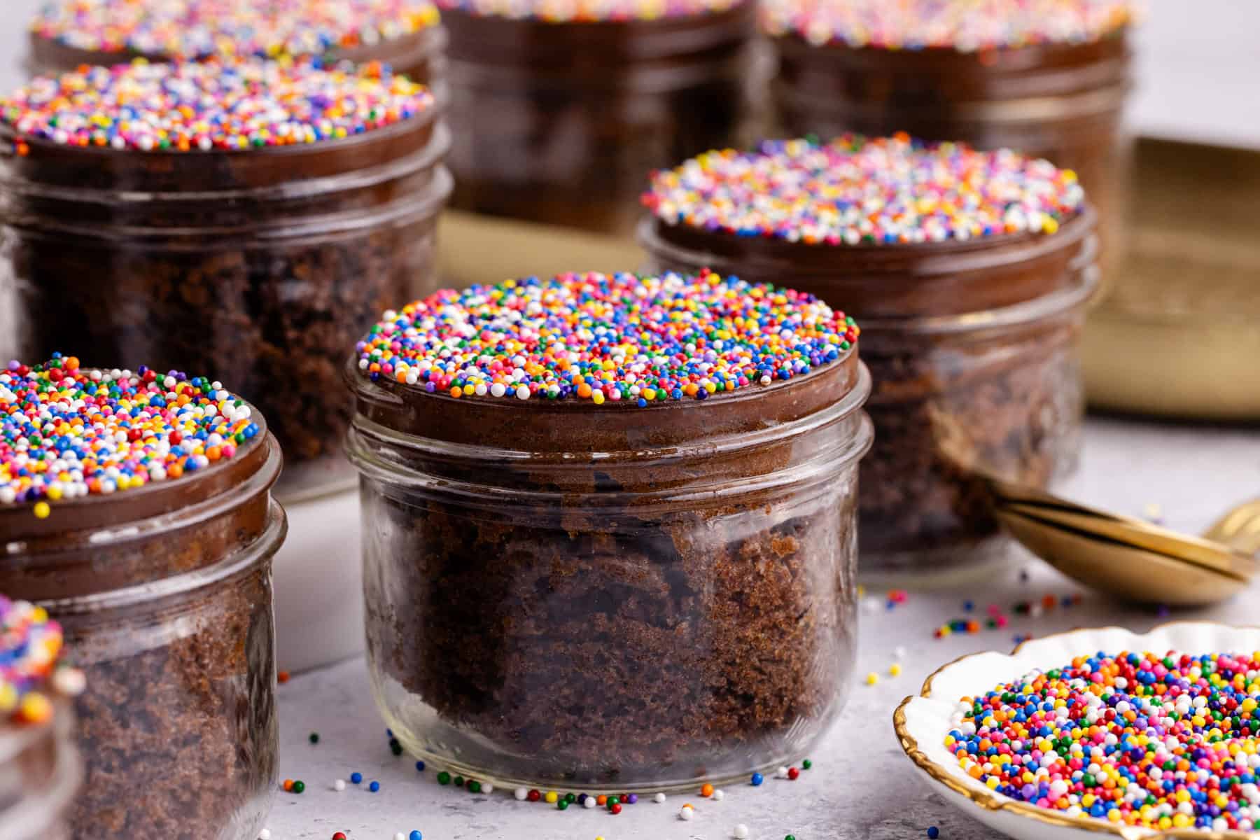 Chocolate Viral Dot Cakes in jars on a counter with sprinkles all around