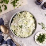 Creamy Cucumber Salad in a bowl with herbs around