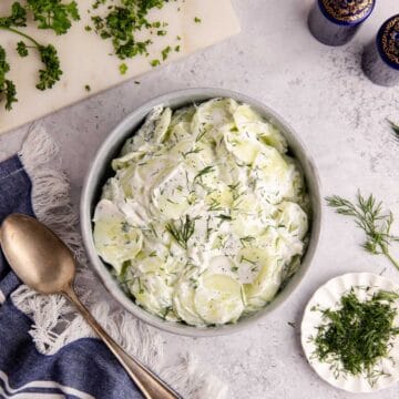 Creamy Cucumber Salad in a bowl with herbs around