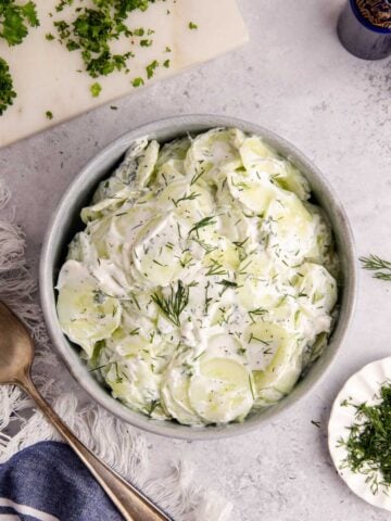 Creamy Cucumber Salad in a bowl with herbs around