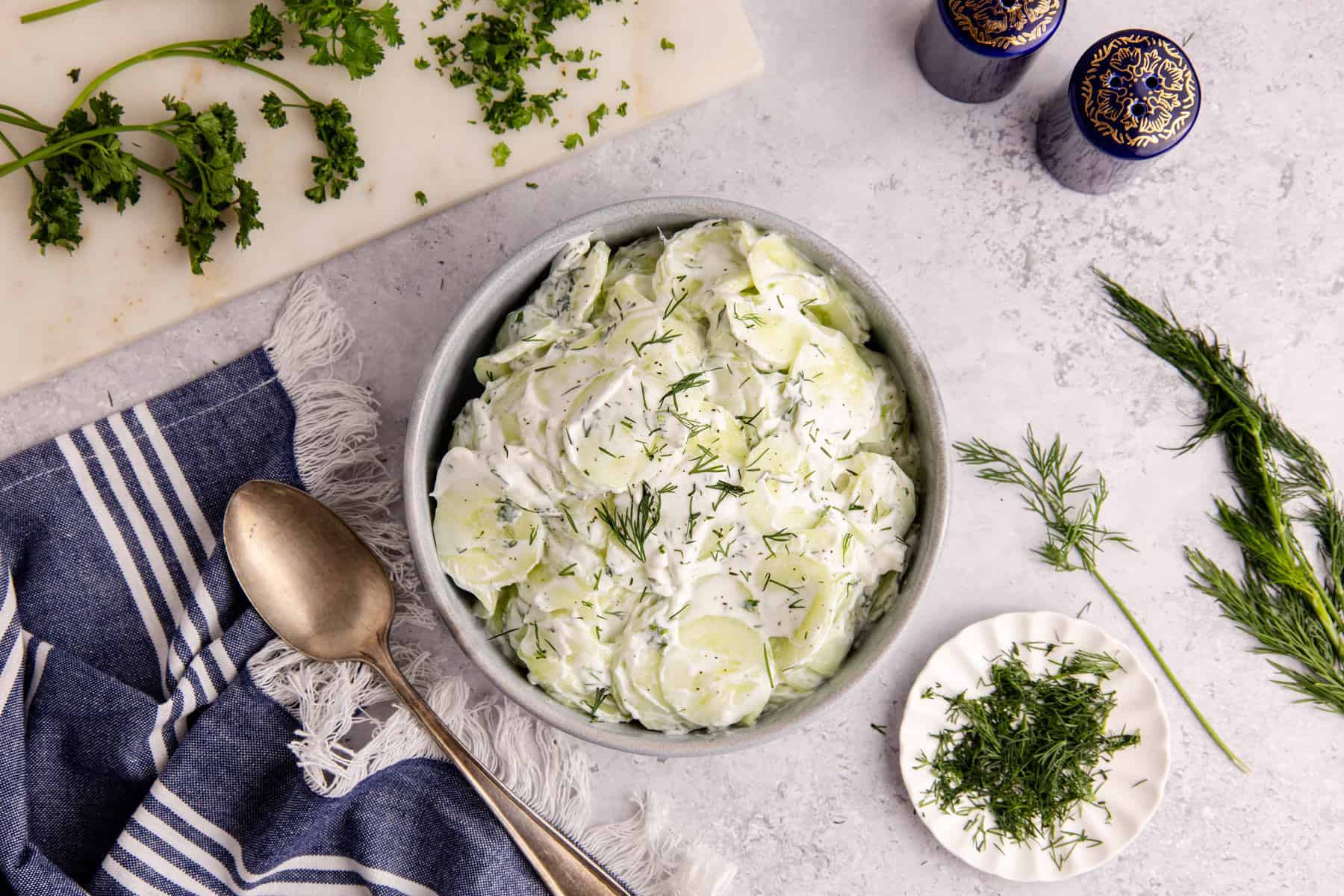 Creamy Cucumber Salad in a bowl with herbs around