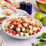 Watermelon Feta Salad in a serving bowl on a counter with limes and a watermelon in the back