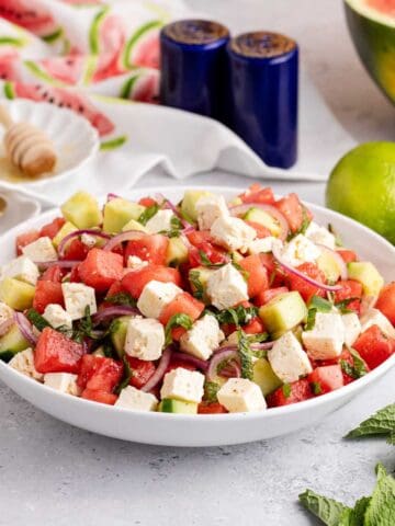 Watermelon Feta Salad in a serving bowl on a counter with limes and a watermelon in the back