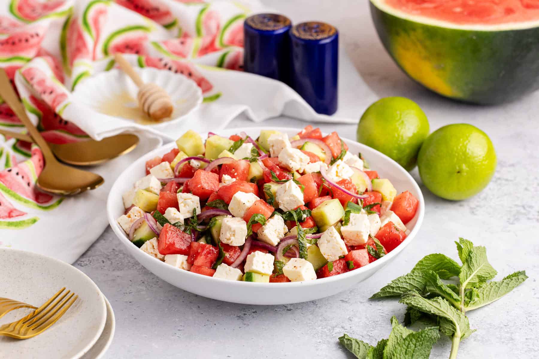 Watermelon Feta Salad in a serving bowl on a counter with limes and a watermelon in the back