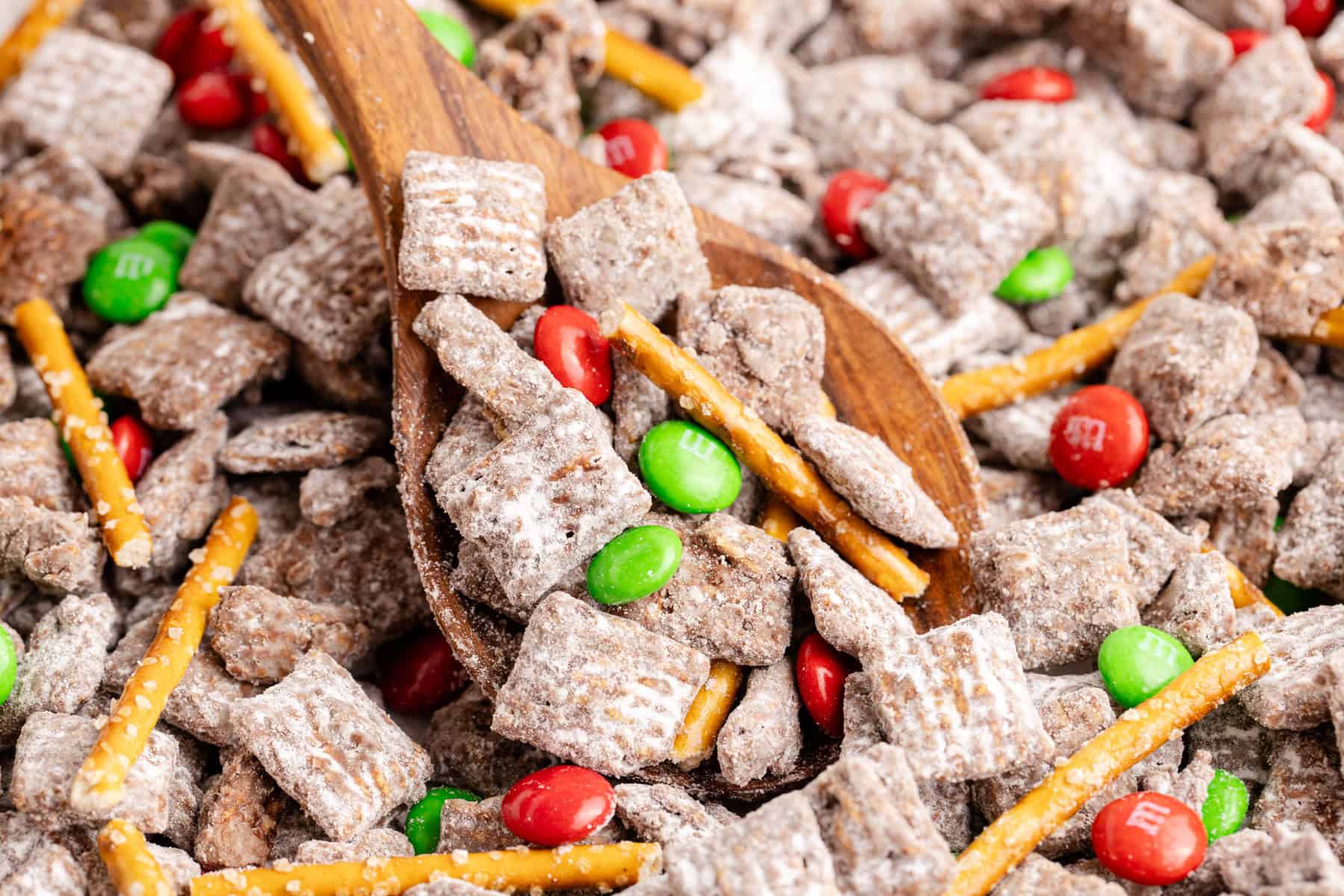 Christmas Puppy Chow on a baking sheet with a serving spoon lifting some up