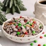 Christmas Puppy Chow in a festive bowl with M&Ms on and around
