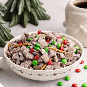 Christmas Puppy Chow in a festive bowl with M&Ms on and around
