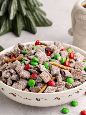 Christmas Puppy Chow in a festive bowl with M&Ms on and around