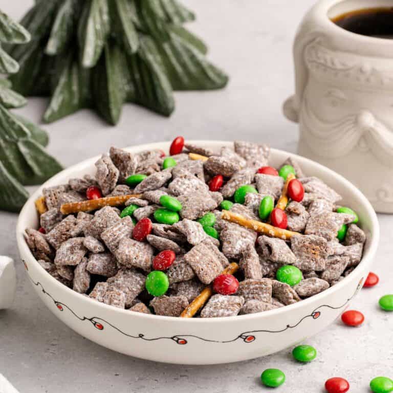 Christmas Puppy Chow in a festive bowl with M&Ms on and around