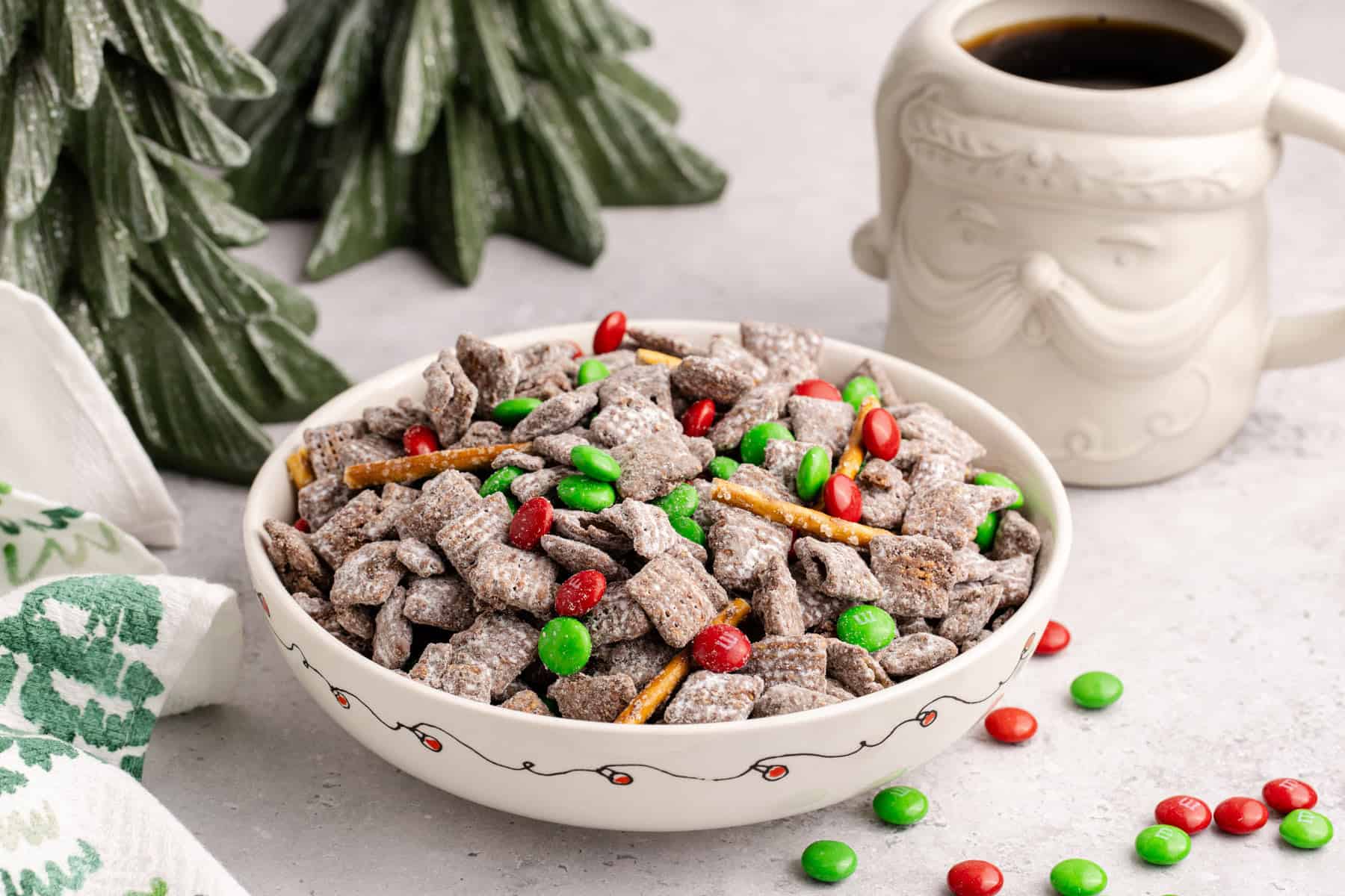 Christmas Puppy Chow in a festive bowl with M&Ms on and around