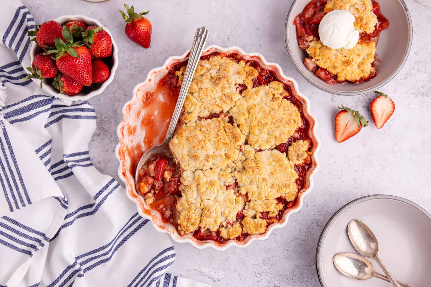 Gluten Free Strawberry Cobbler on a counter with berries and a bowl filled in the back