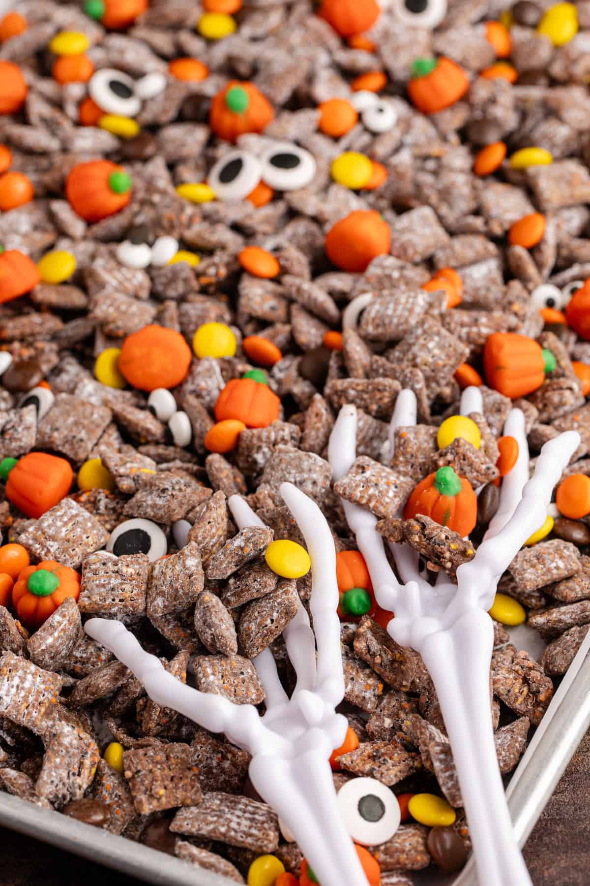 Halloween Puppy Chow on a baking sheet with skeleton hands holding some
