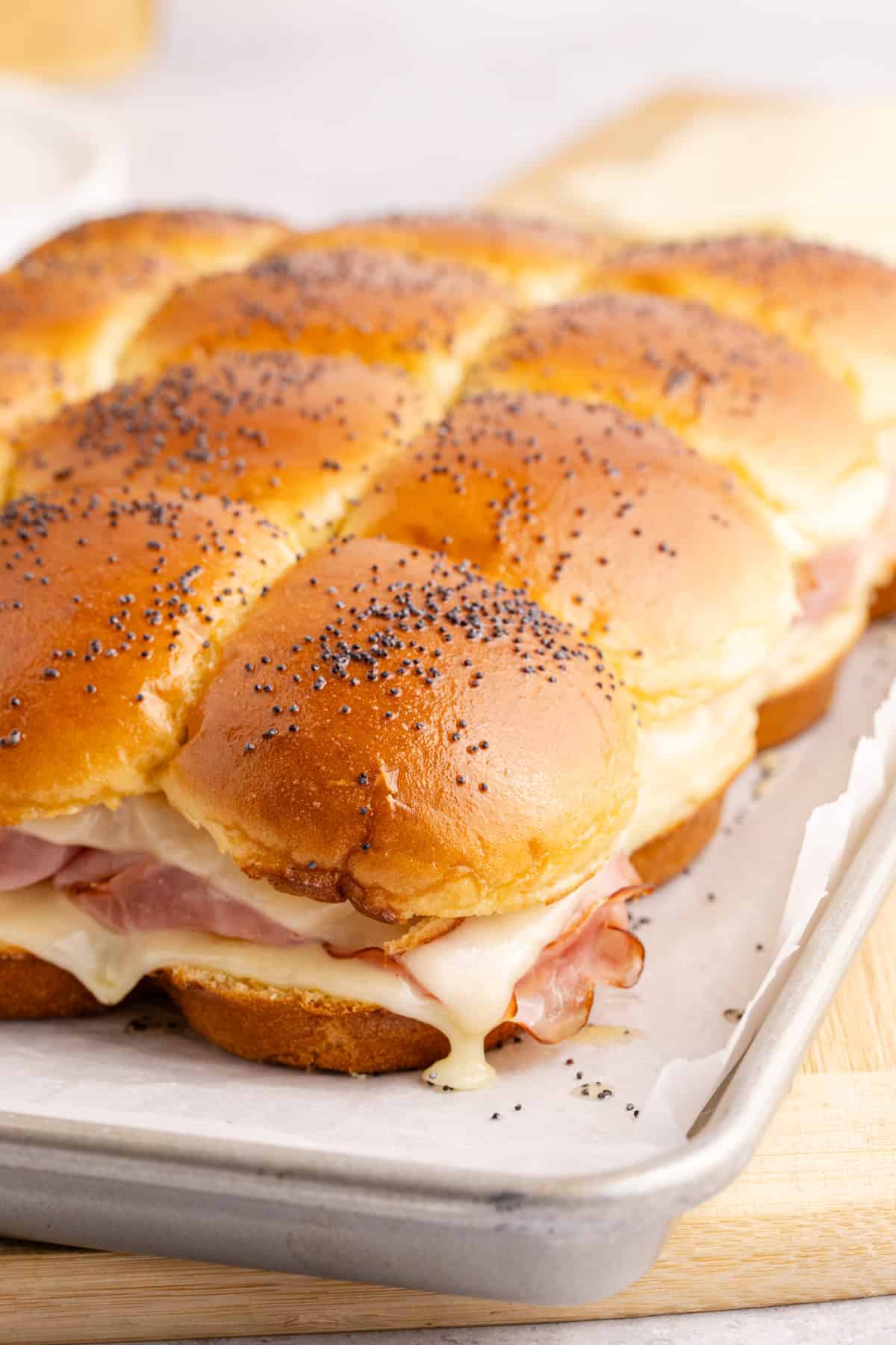 ham and cheese sliders on hawaiian roll buns topped with poppyseeds on sheet pan