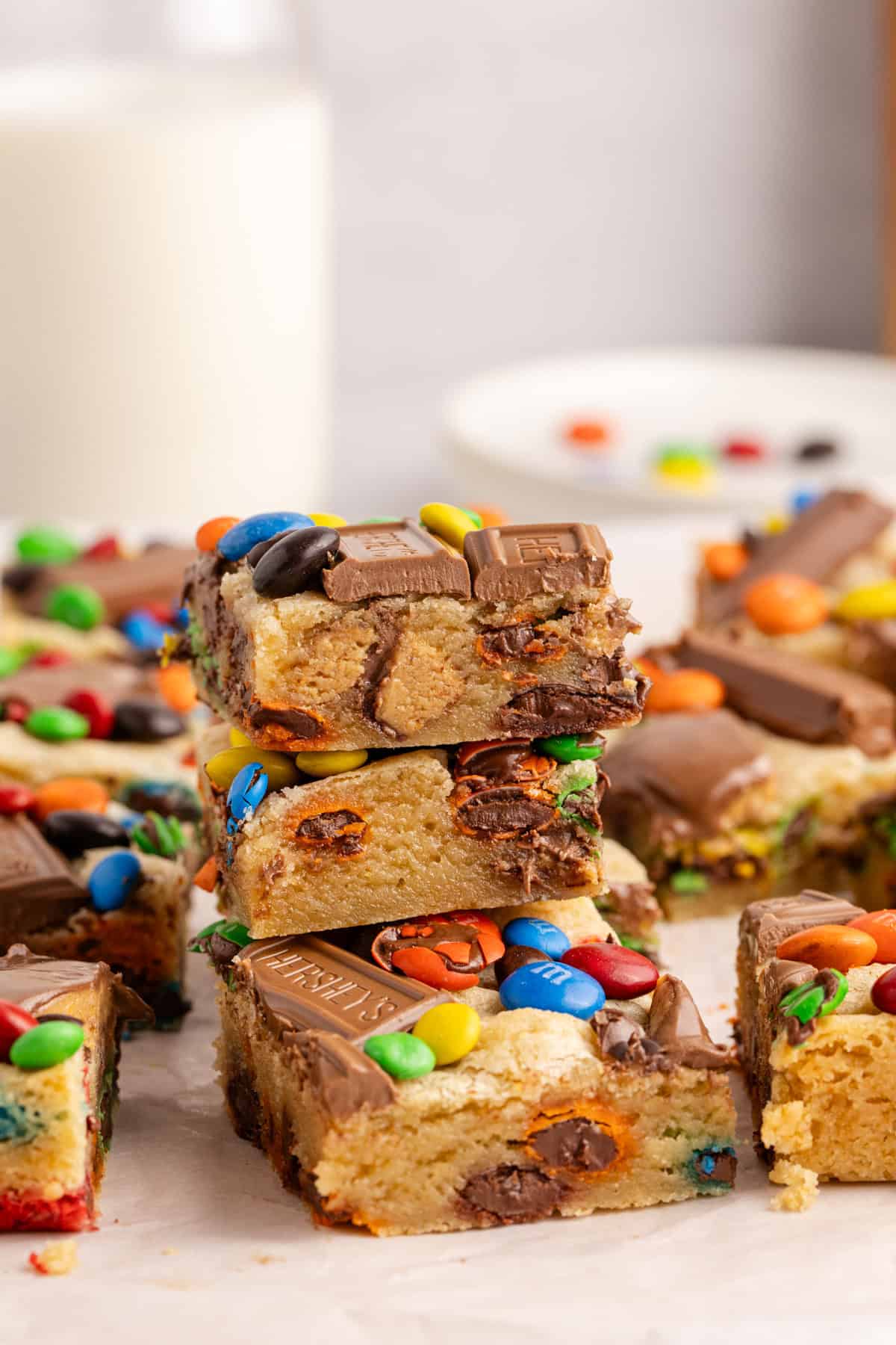 Leftover Candy Cookie Bars stacked on a counter with milk in the back