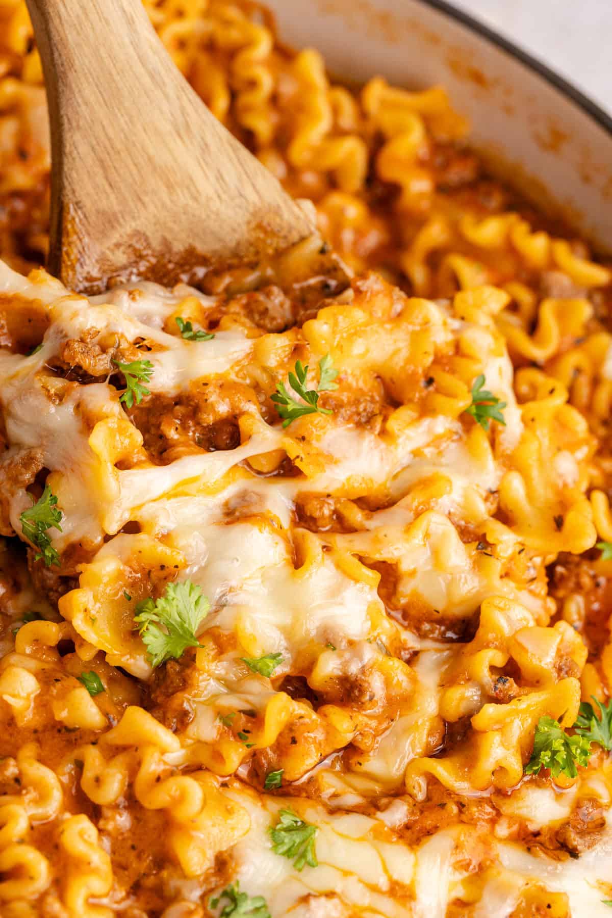 wooden spoon lifting noodles in one pan lazy lasagna
