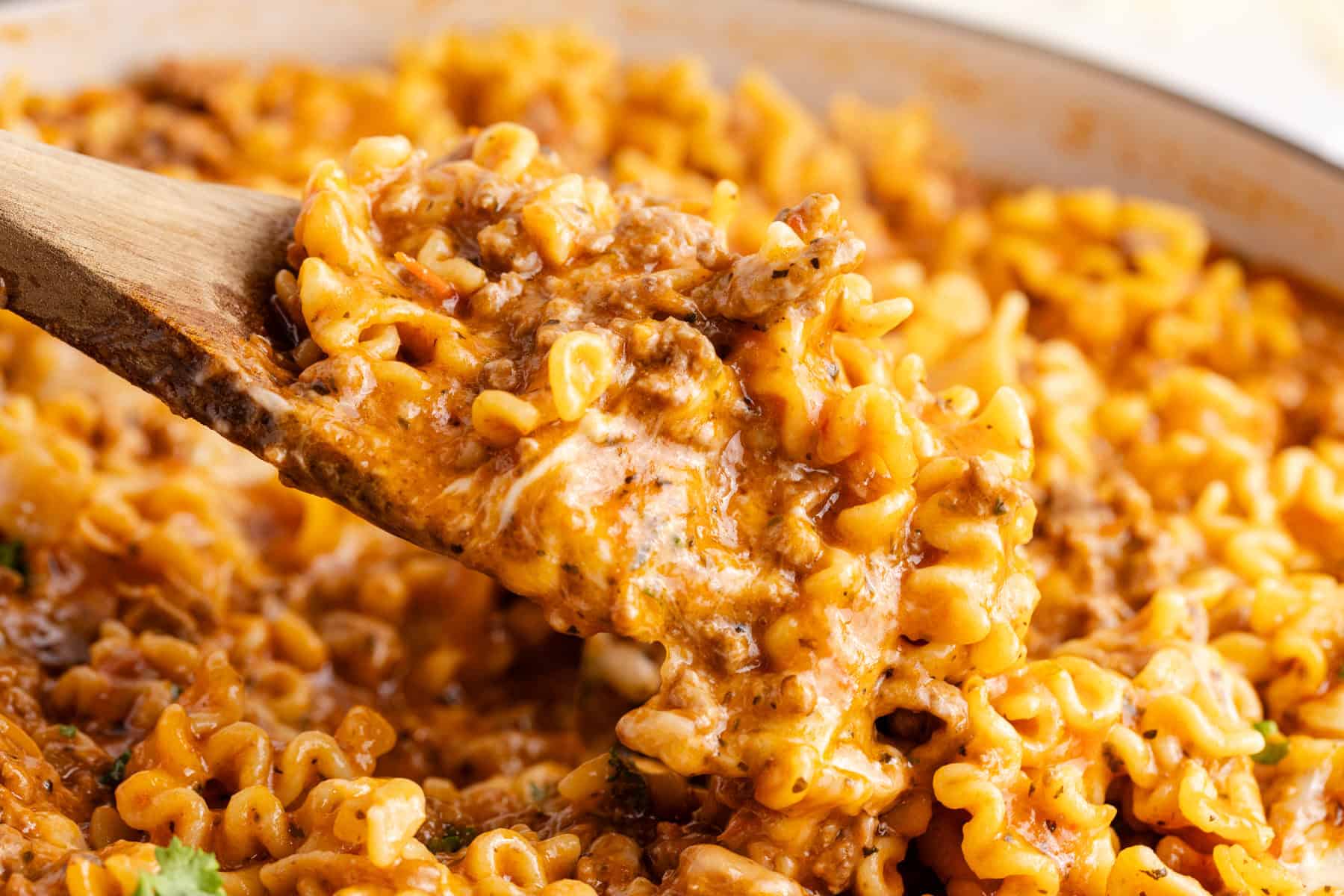 wooden spoon lifting noodles in one pan lazy lasagna