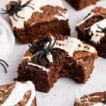Spiderweb Brownies with plastic spiders on top on a counter and a bite taken from one