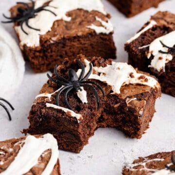 Spiderweb Brownies with plastic spiders on top on a counter and a bite taken from one