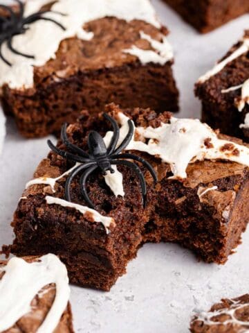 Spiderweb Brownies with plastic spiders on top on a counter and a bite taken from one