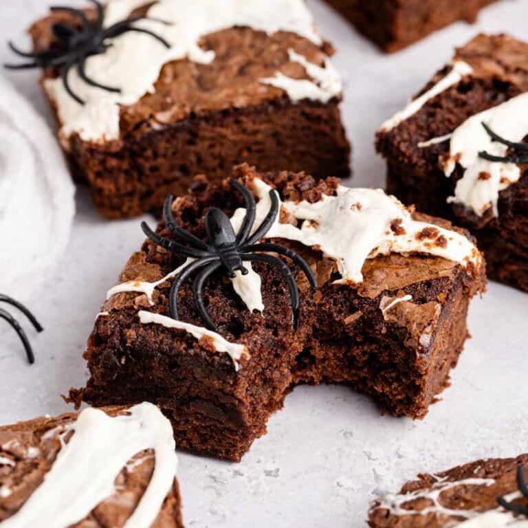 Spiderweb Brownies with plastic spiders on top on a counter and a bite taken from one
