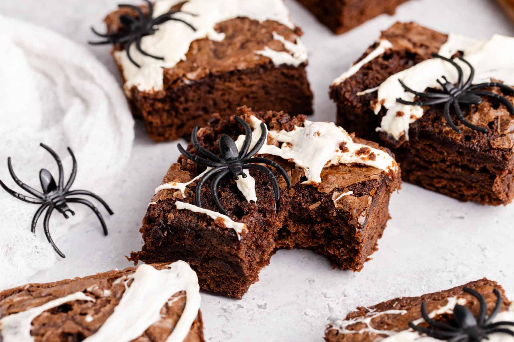 Spiderweb Brownies with plastic spiders on top on a counter and a bite taken from one
