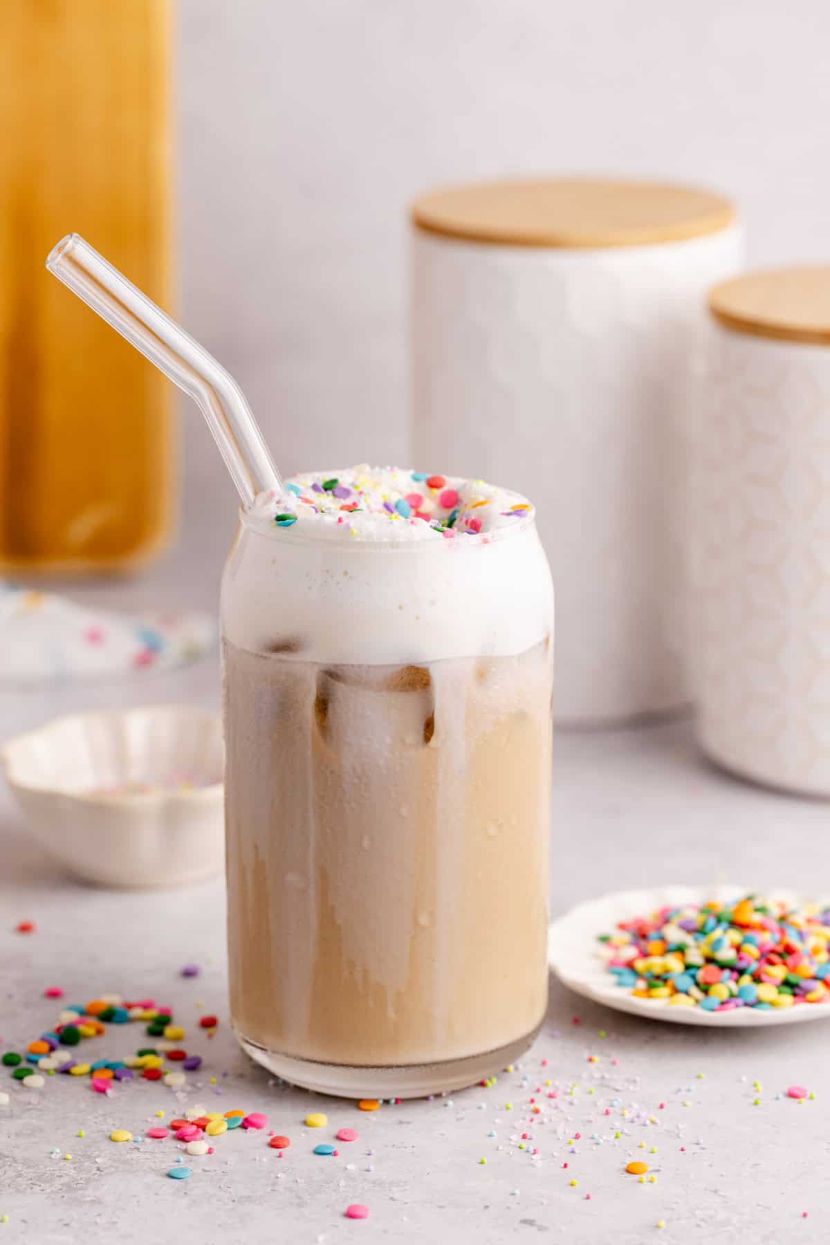 Whimsical Latte with sprinkles on top off the cold foam and canisters in the back