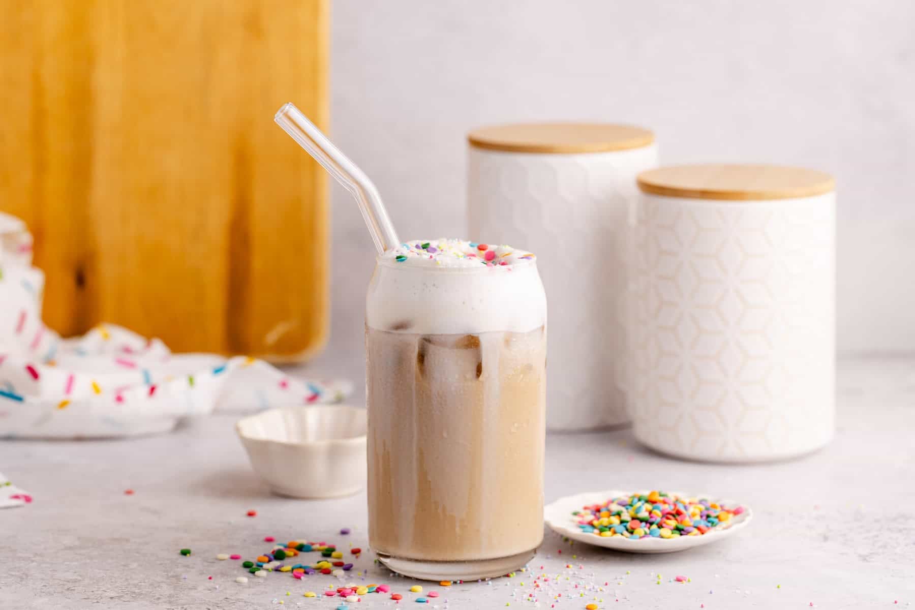 Whimsical Latte with sprinkles on top off the cold foam and canisters in the back