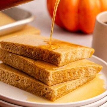 Pumpkin Spice Sheet Pan Pancakes stacked on a plate with maple syrup pouring