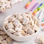 Cake Batter Puppy Chow in a bowl with candles in the back and more cereal in the front