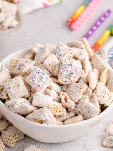 Cake Batter Puppy Chow in a bowl with candles in the back and more cereal in the front